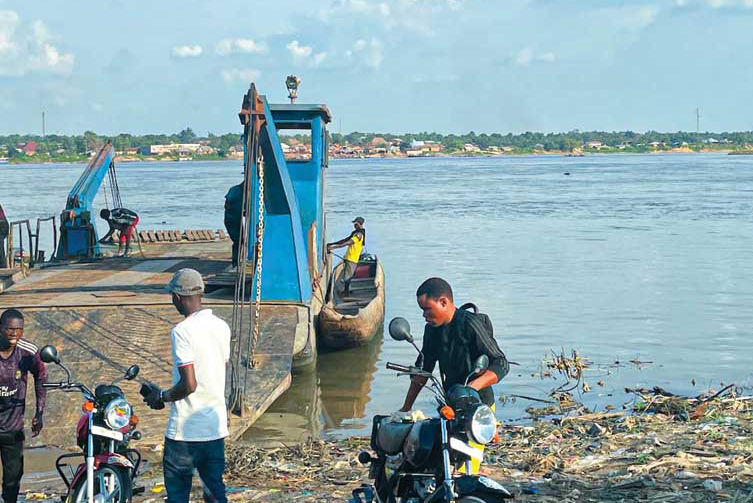 Before heading to Mirundu, the author and his colleague, Valery, first had to take a barge across the Congo River. The engine was broken, so a dugout canoe with a small motor was strapped to either side.
