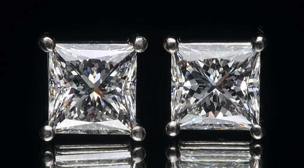 Two square diamond earrings a are sitting next to each other with a black background.