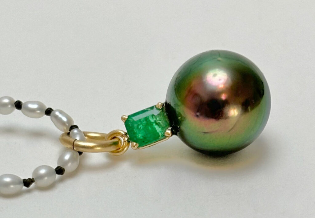 Close-up of a pendant made of a pearl and emerald.