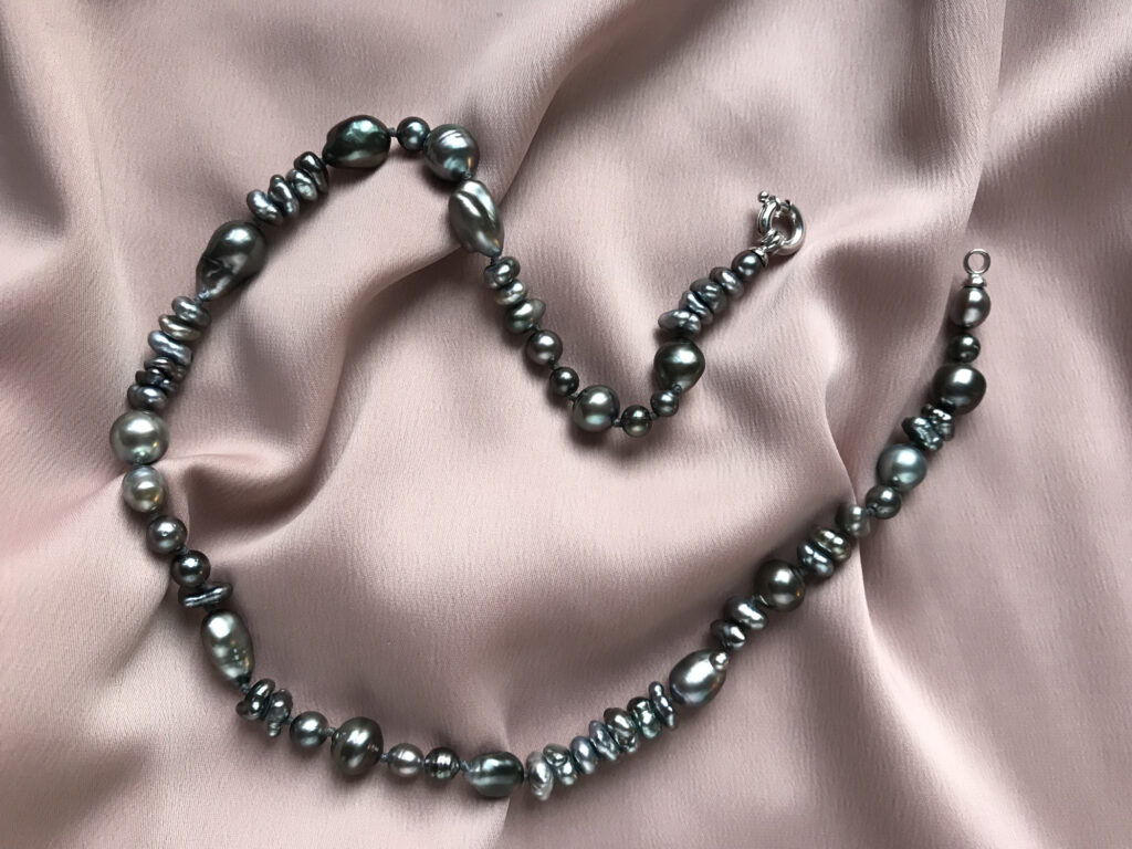 A dark pearl necklace placed on silk.