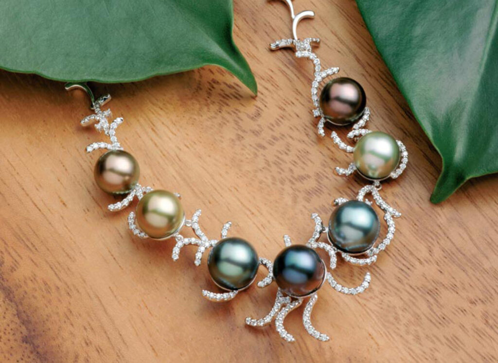 Necklace of different coloured pearls and diamonds lies on a plank of wood.