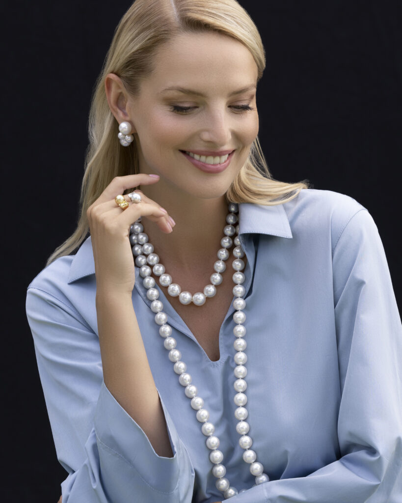 A white female model in a blue tailored shirt with a string of pearls and pearl earrings.