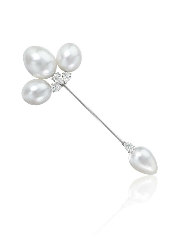 A brooch with three large pearls at the top with another pearl at the bottom on a white background.