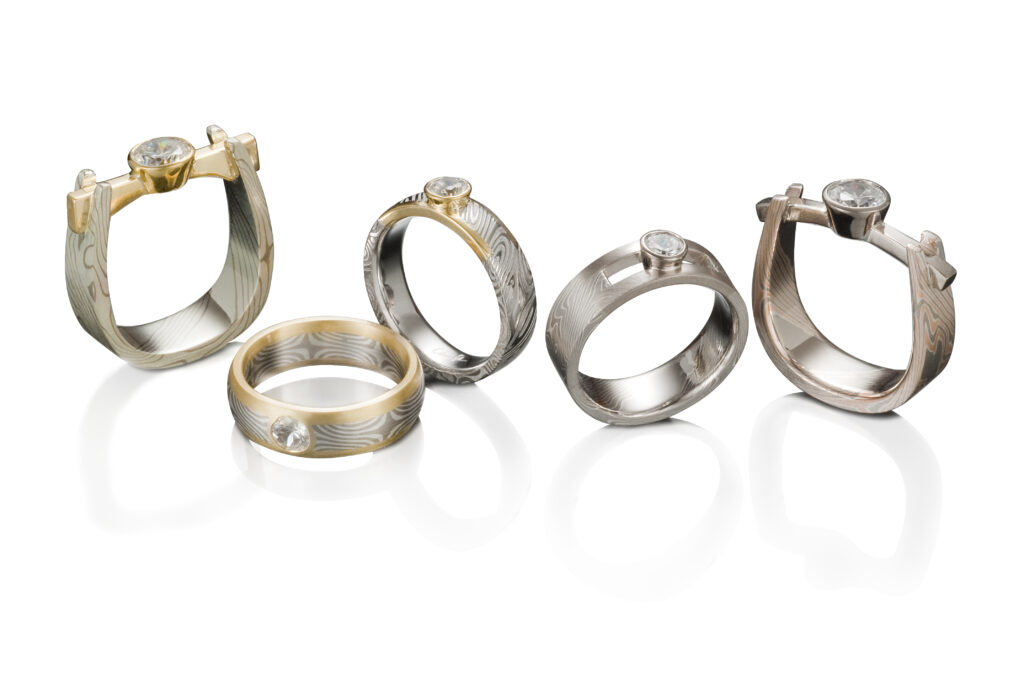 Five silver and gold engagement rings are situated horizontally.