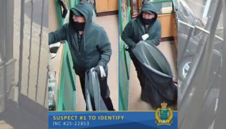 Surveillance footage of a white suspect in a green hoody and cap with glasses holding a garbage bag at the scene of robbery.