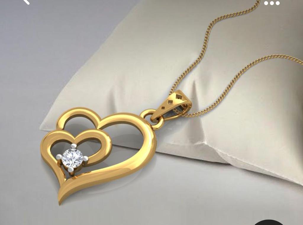A gold double heart-shaped pendant with a diamond in the centre of the smaller heart on a gold chain, draped on a satin pillow.
