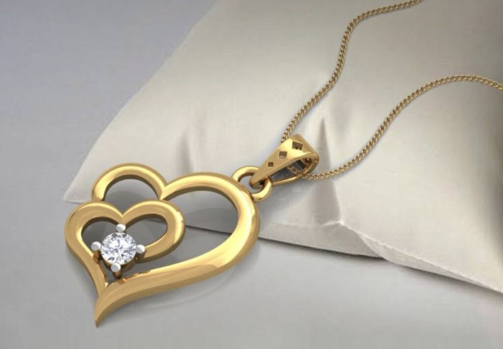 A gold double heart-shaped pendant with a diamond in the centre of the smaller heart on a gold chain, draped on a satin pillow.