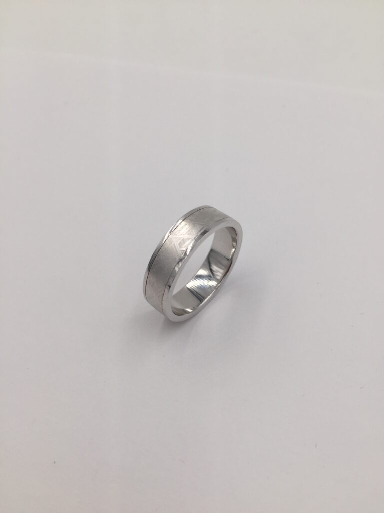 A silver coloured men's ring sits on a gray background.