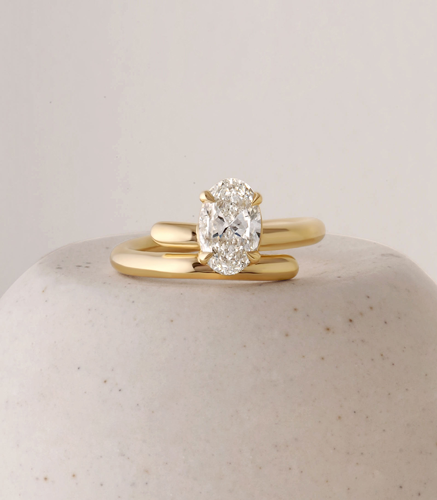 An oval white diamond ring with double yellow gold band.