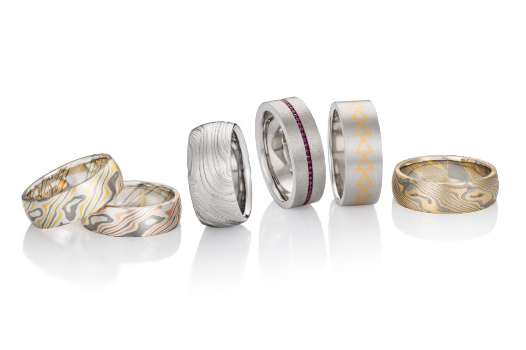 Six men's rings are placed in a row with a white background.