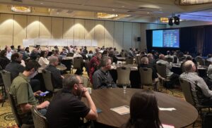 People seated around tables and watching a presentation.