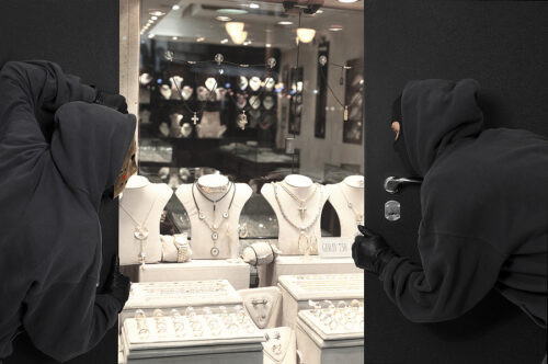 Men wearing masks hide behind door, looking inside a jewelry store.