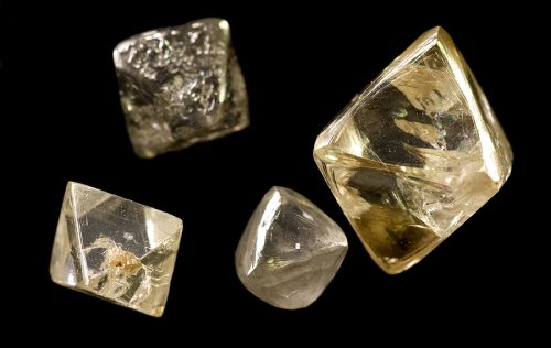 rough uncut diamonds showing crystalline structure, facets and imperfections on a black background