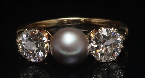 close up of antique ring with pearl in the middle and diamonds on side