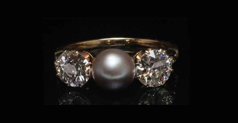 close up of antique ring with pearl in the middle and diamonds on side