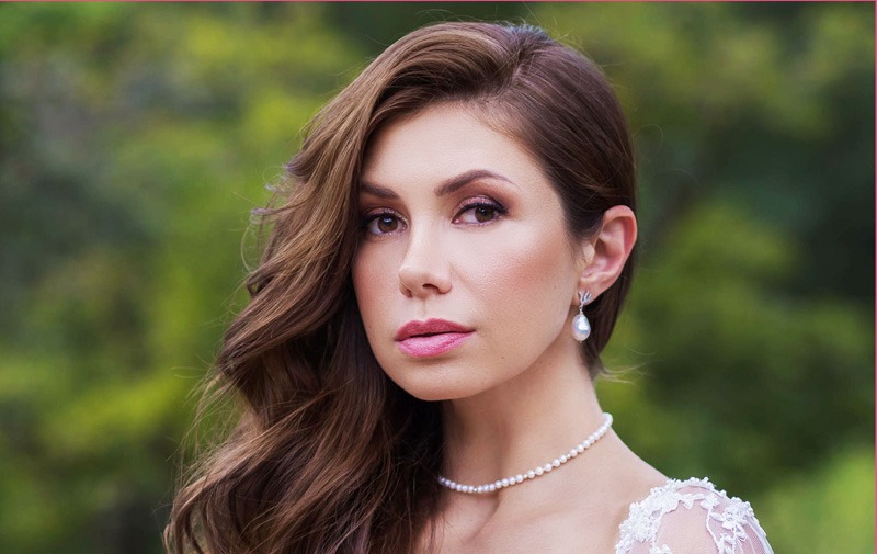 woman with long brown wavy hair and pearl necklace