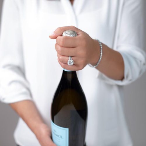 person holding champagne bottle with silver ring and bracelet on left hand