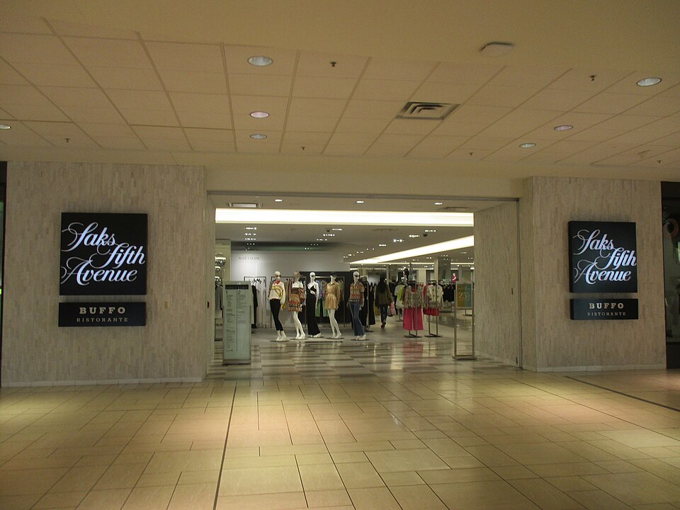 Entrance to Saks Fifth Avenue store in a mall, displaying mannequins dressed in fashionable clothing.