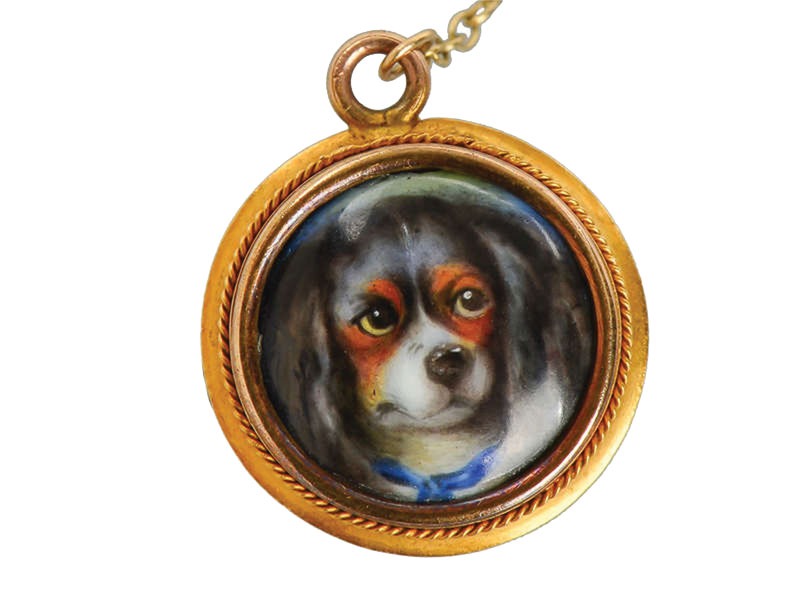 Round gold-framed pendant with a hand-painted enamel portrait of a Cavalier Spaniel wearing a blue bow.