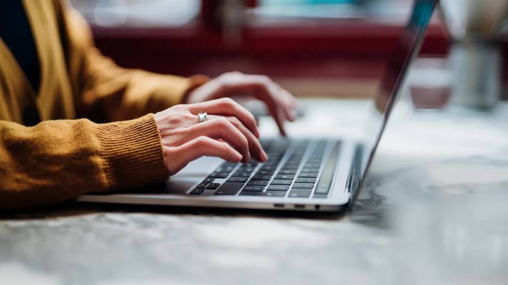 Close-up of a person in a mustard cardigan typing on a laptop, a reminder of the everyday habits, like strong passwords and careful clicking, that keep personal data secure.